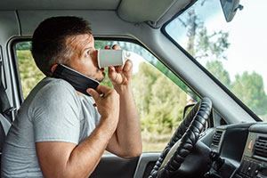 A man drinking coffee and on his phone whilst driving for work