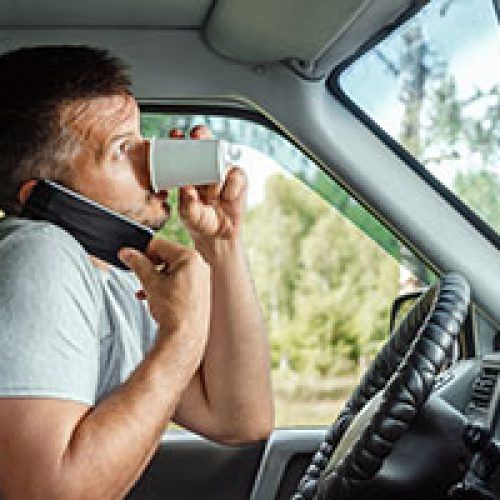  A man drinking coffee and on his phone whilst driving for work