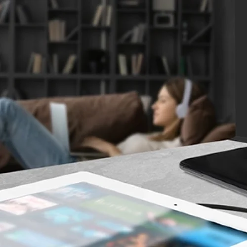 Lady using a laptop wearing headphones in the background in the foreground are 2 devices on charge from BG Electrical evolve decorative light switches and sockets